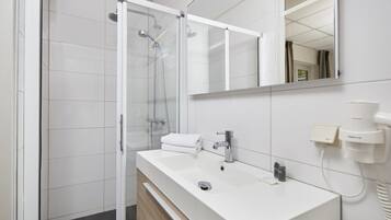 Un baño moderno con cabina de ducha de vidrio, un lavabo blanco con espejo y un perchero para toallas.