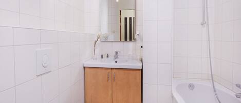 A compact bathroom with a white toilet, a sink with a mirror above it, wooden cabinets, and a bathtub with a showerhead.