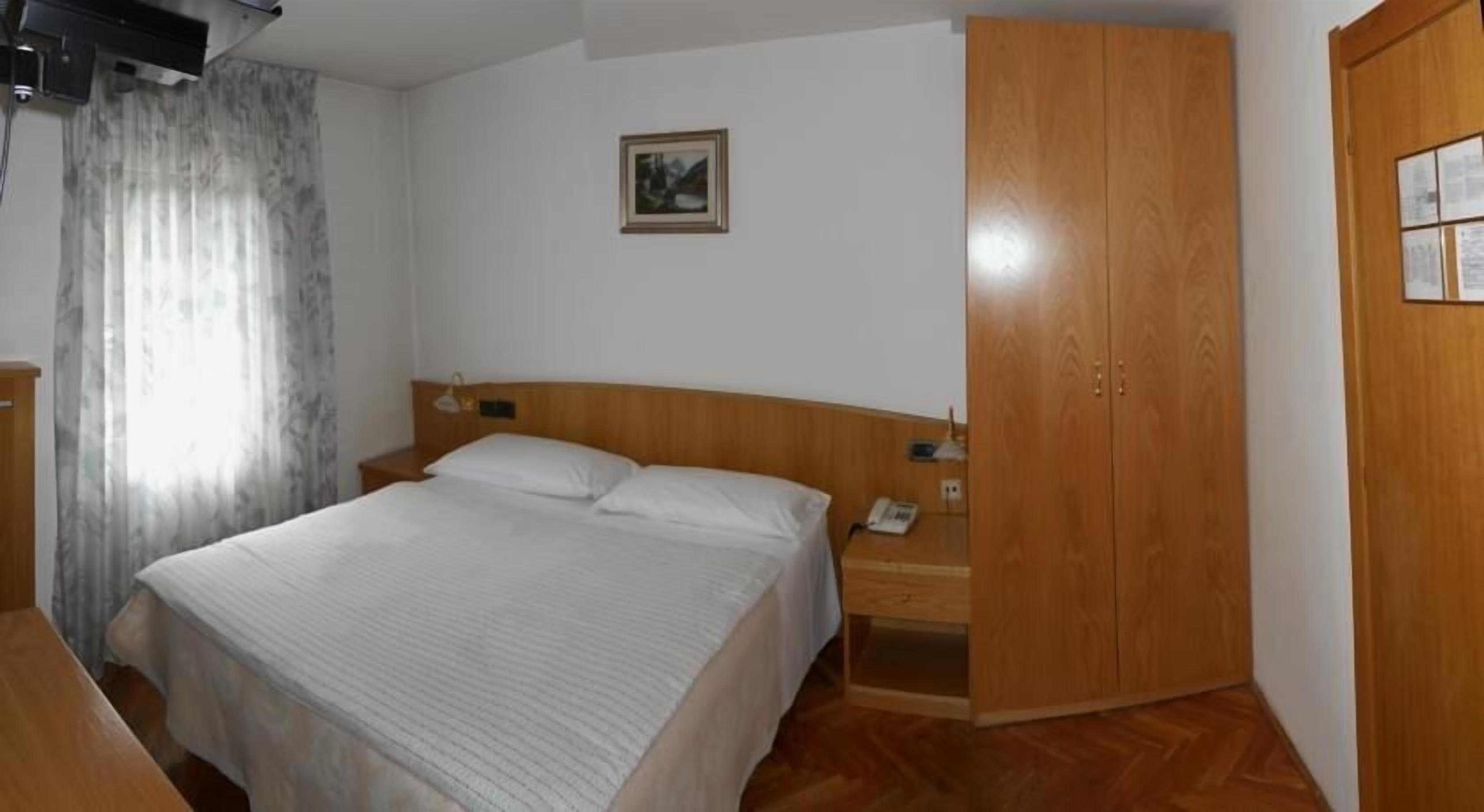 A hotel room with a bed, wooden wardrobe, and a nightstand with a lamp.