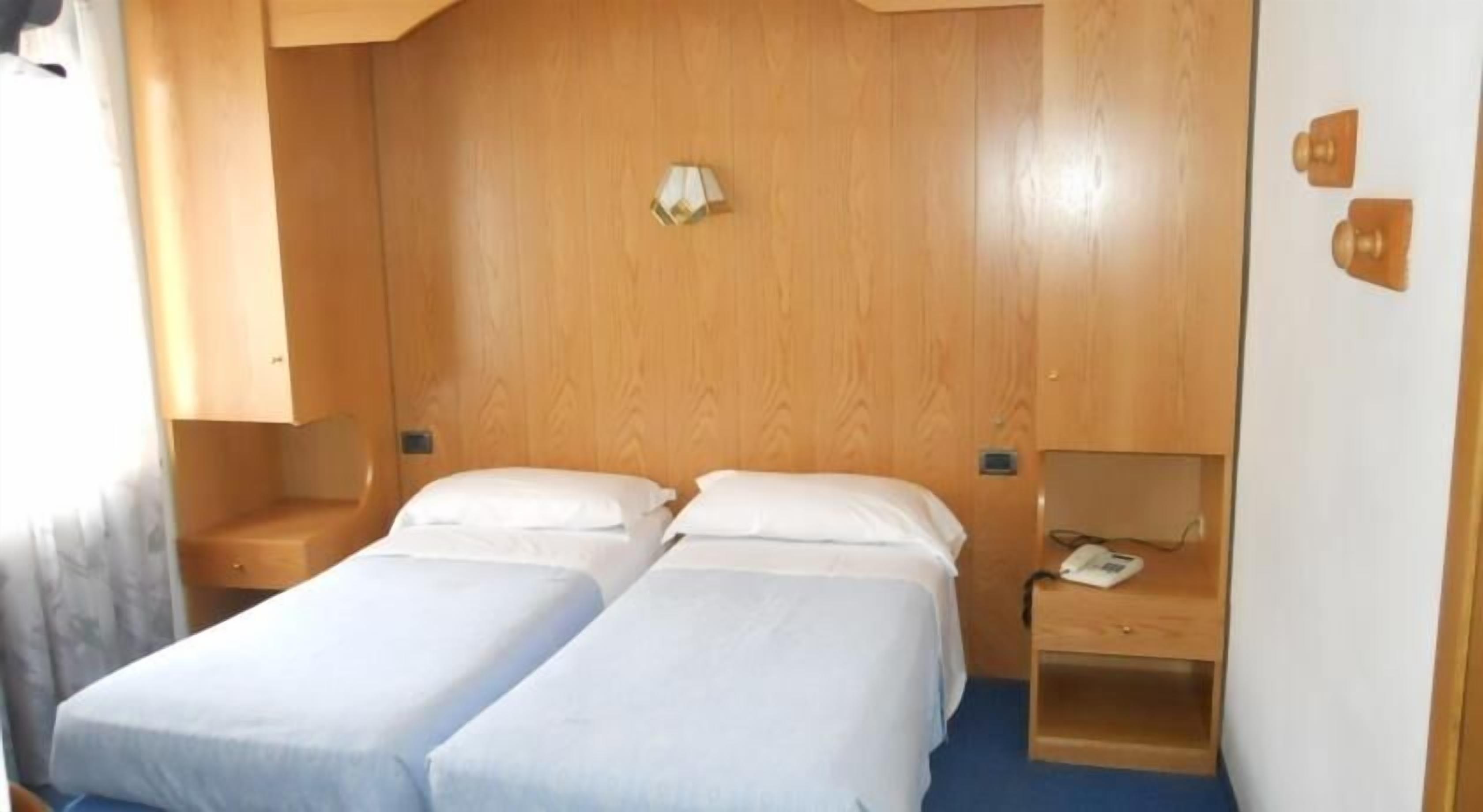 Una camera compatta con due letti singoli, una testiera in legno, comodini e una scrivania con una sedia.