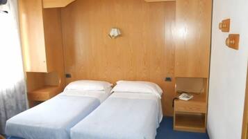 Una camera compatta con due letti singoli, una testiera in legno, comodini e una scrivania con una sedia.