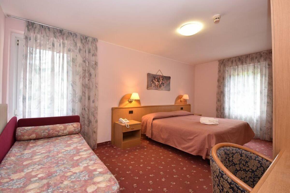 A hotel room with a single bed, a sofa bed, a chair, and two bedside tables with lamps.