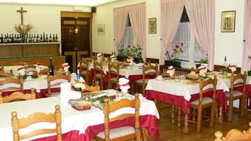 A dining area with multiple tables set for meals, wooden chairs, and a bar area with bottles.