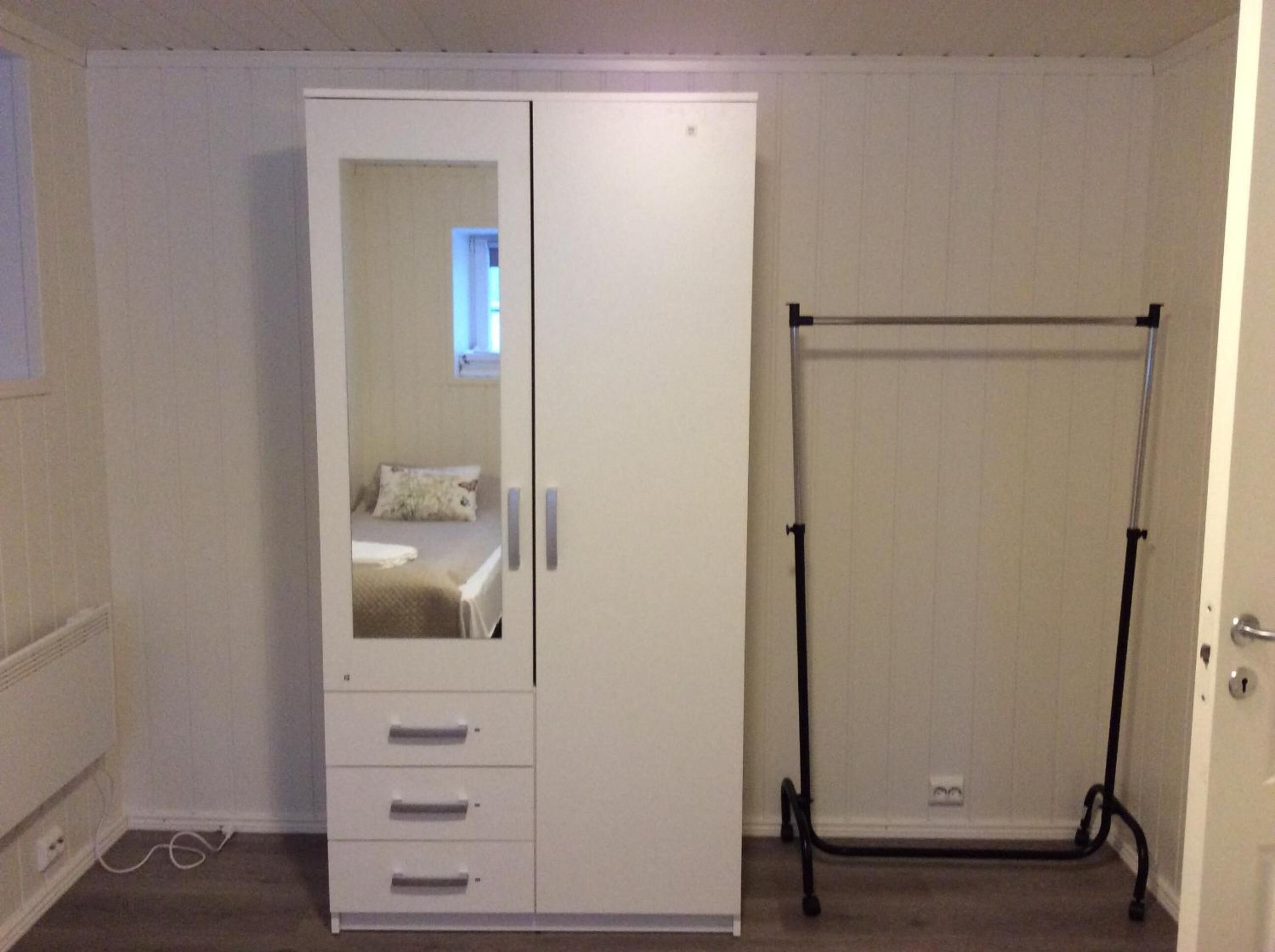 Una habitación con un armario blanco, un espejo y una estantería de metal negro.