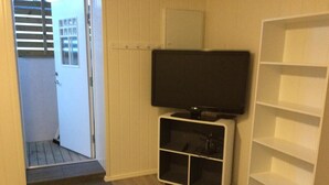A room with a television on a stand, a white shelving unit, and a door leading to a balcony. - Barents Frokosthotell (South Varanger)