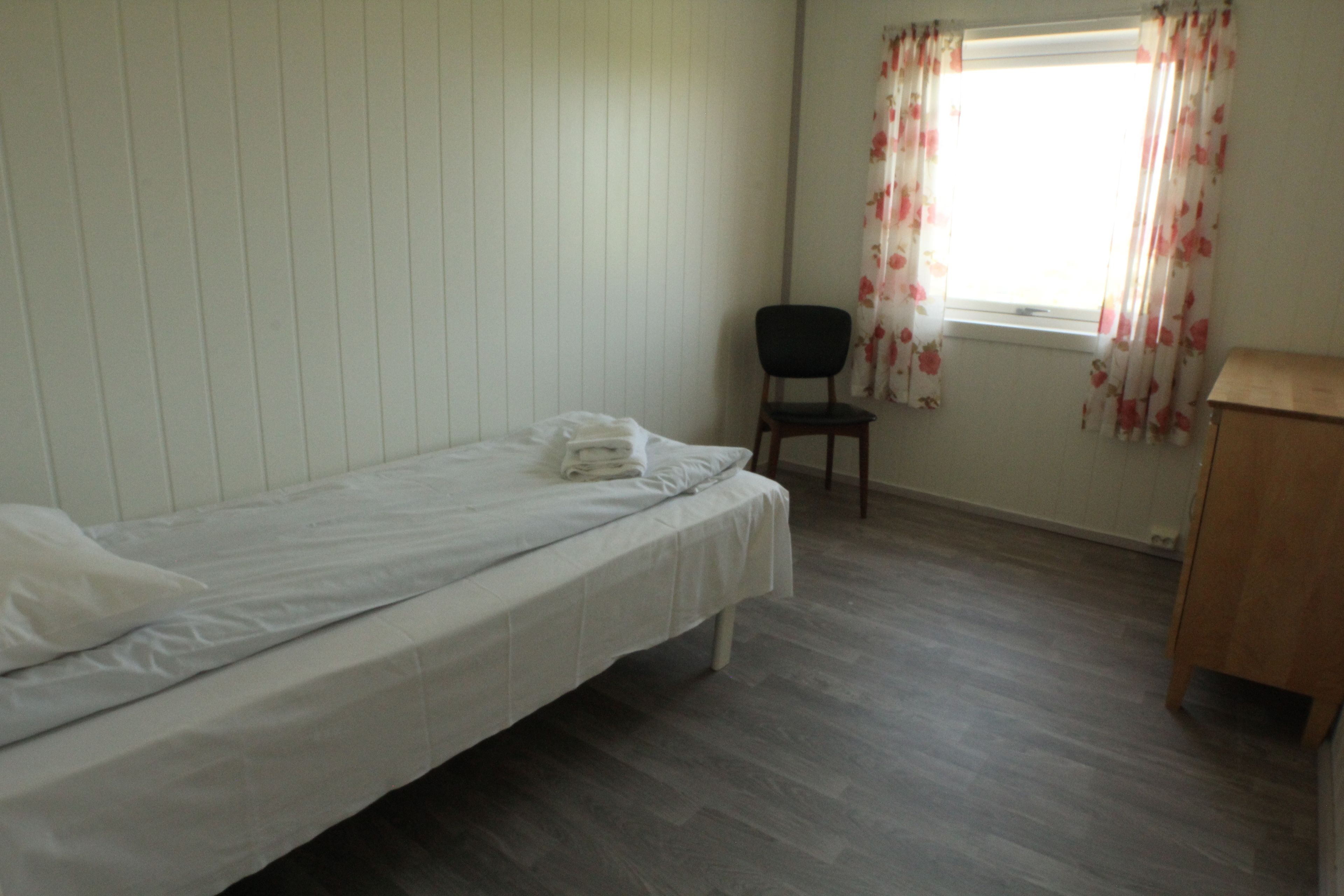 Una habitación pequeña y limpia con una cama individual, una silla y un escritorio de madera.