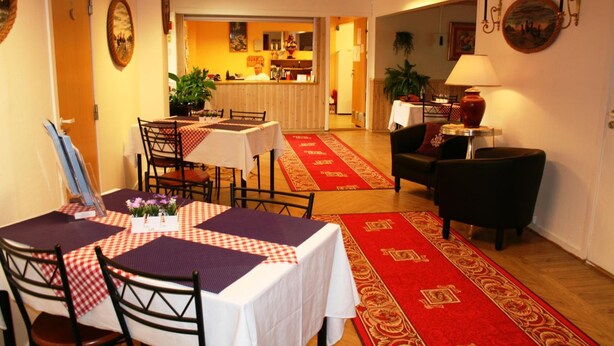 A dining area with a table set for four, a red carpet, and a bar in the background. - Barents Frokosthotell (South Varanger)