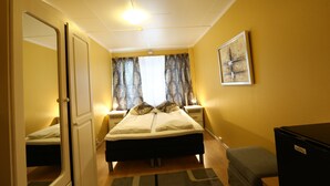 A bedroom with a bed, bedside tables, a mirror, a window with curtains, and a painting on the wall. - Barents Frokosthotell (South Varanger)