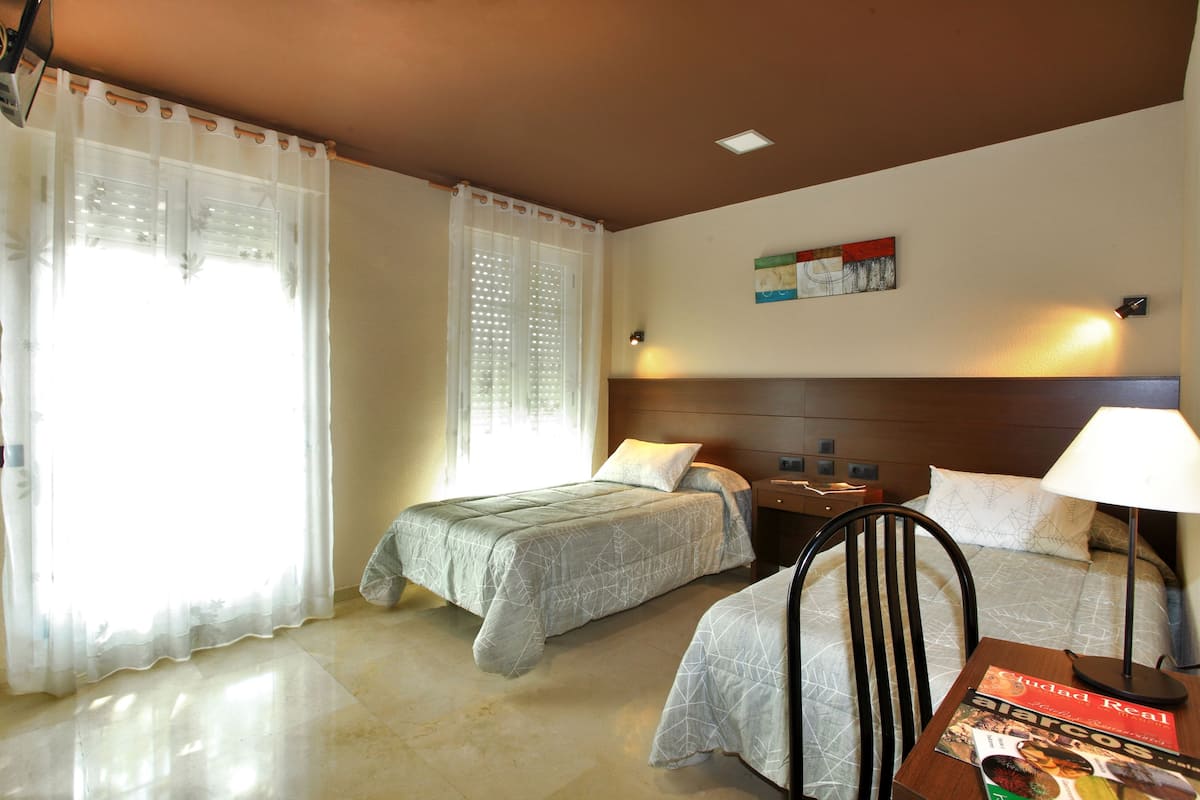 Una habitación de hotel con dos camas, una mesita de noche, una silla y una mesa con una revista.