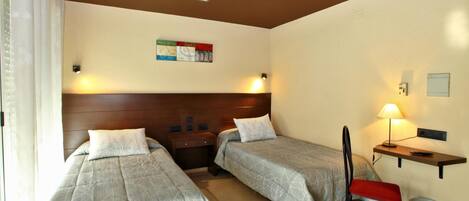 Une chambre d’hôtel avec deux lits simples, une table de chevet, une chaise, un bureau et une lampe fixée au mur.