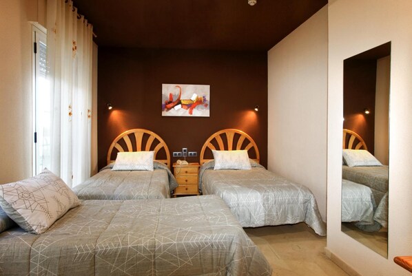 Une chambre d’hôtel avec deux lits, un grand miroir, un tableau au mur et une fenêtre avec des rideaux.