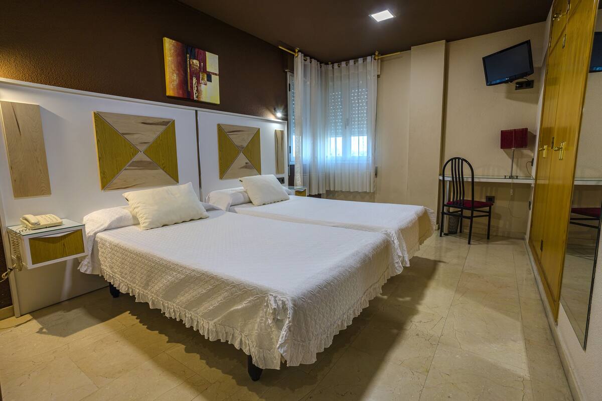 Habitación de hotel con dos camas, un escritorio, una silla, un televisor y un armario.