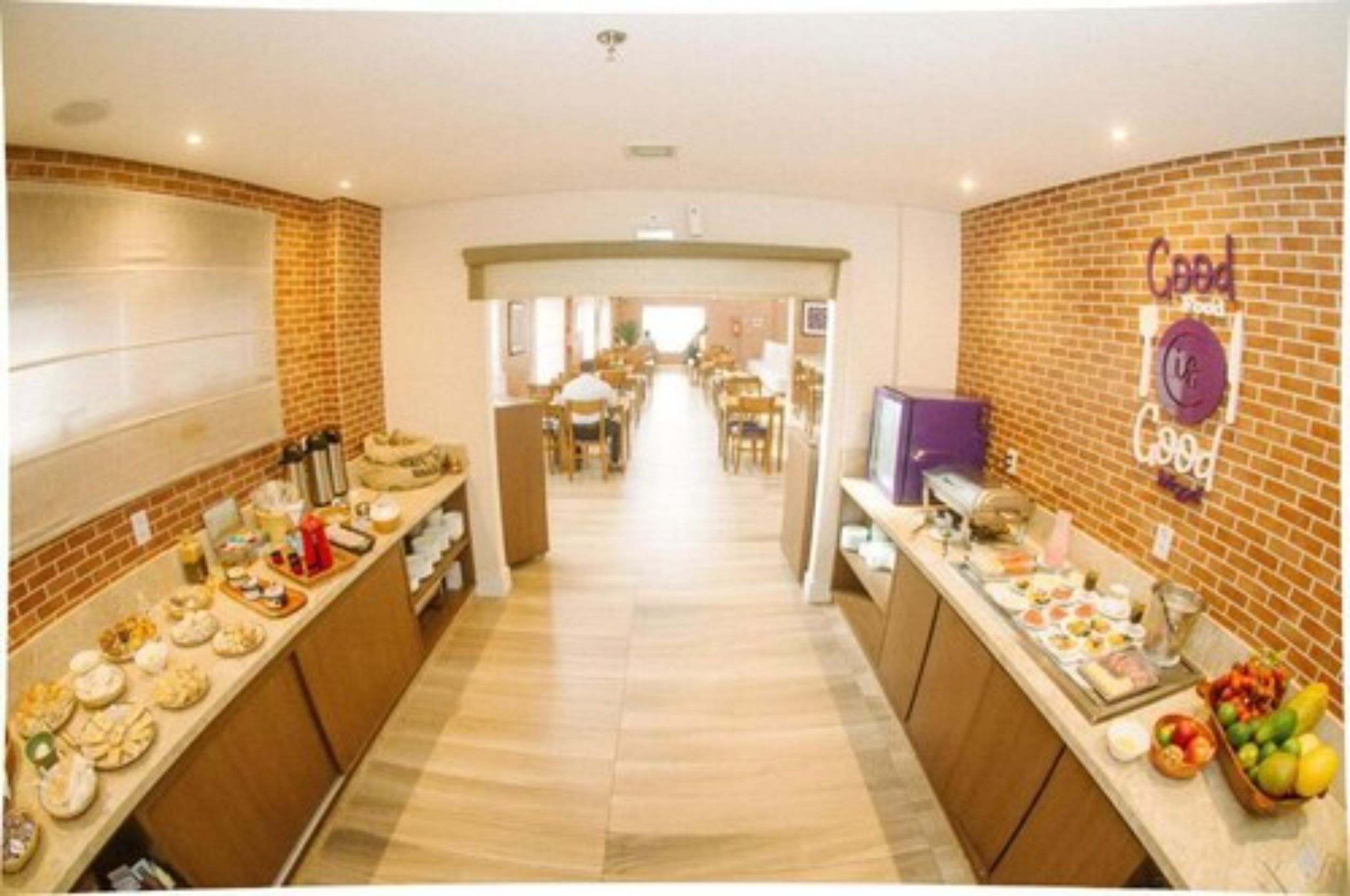 A hotel lobby with a long reception desk, a brick wall with a sign, and a view into the dining area.