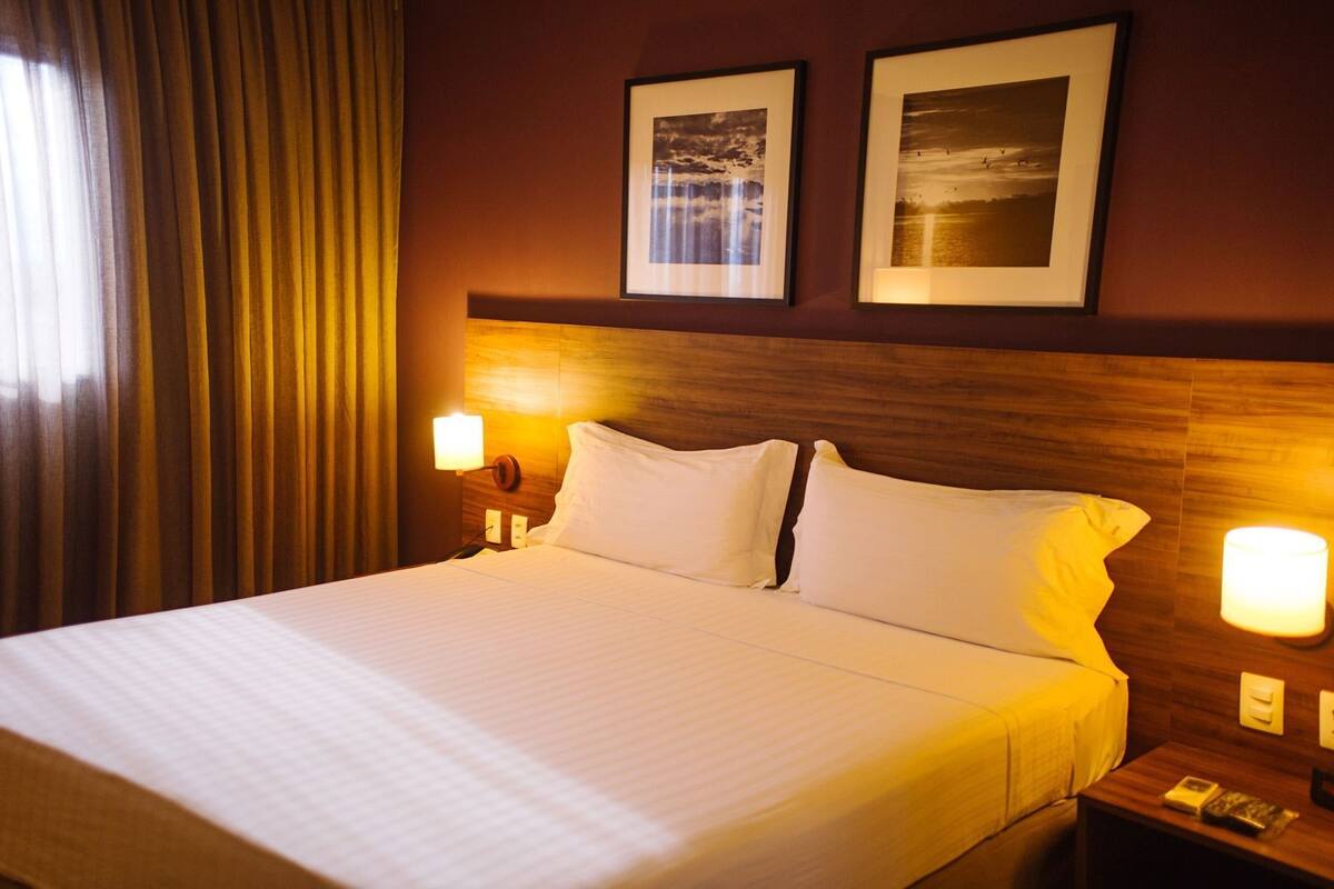 A hotel room with a bed, two bedside lamps, a nightstand, and two framed pictures on the wall.
