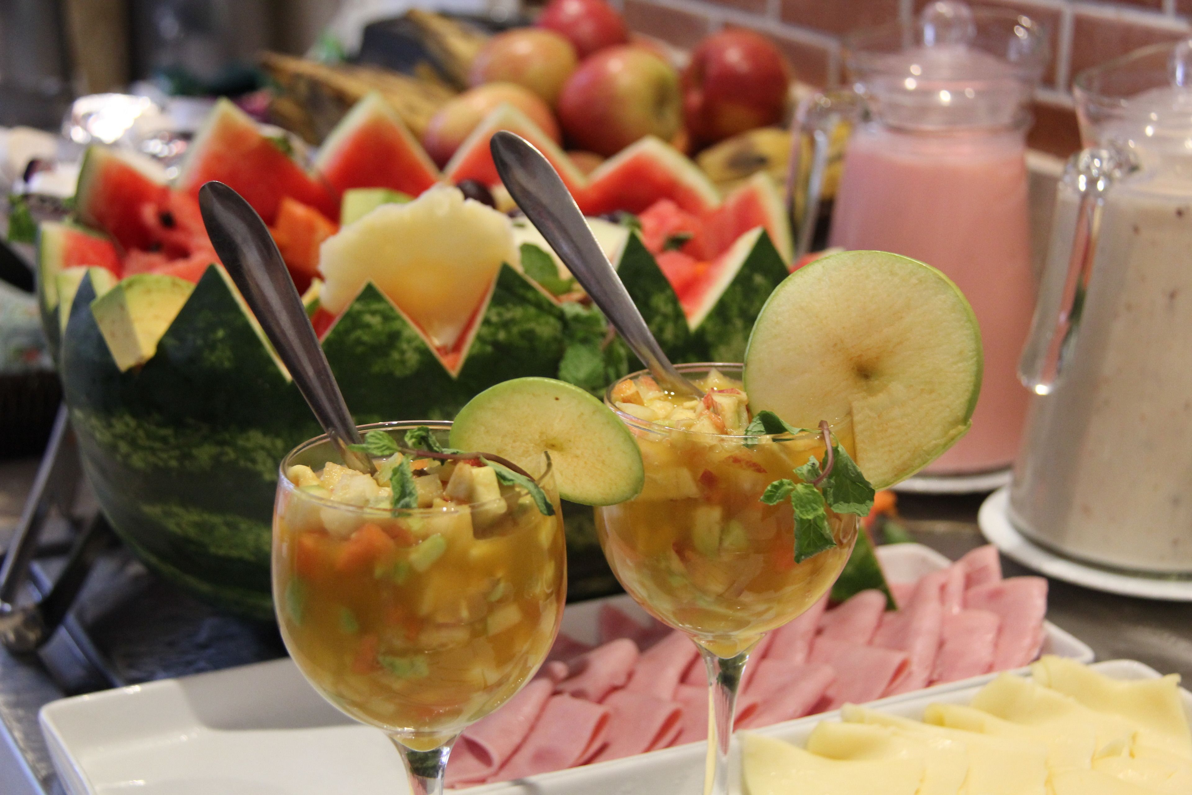 Un buffet con diverse varietà di frutta, un'anguria e un dispenser per bevande.