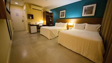 A hotel room with two beds, a desk, a chair, and a small kitchenette.