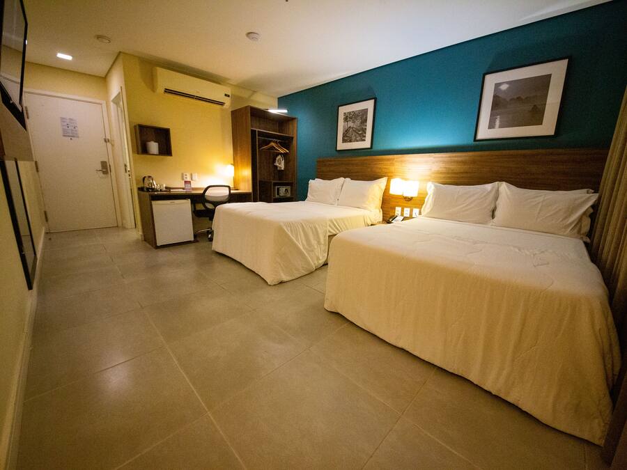 A hotel room with two beds, a desk, a chair, and a small kitchenette.