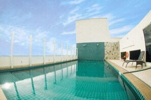 A swimming pool with clear blue water, a white and green tiled wall, and a lounge area with a chair and a table.