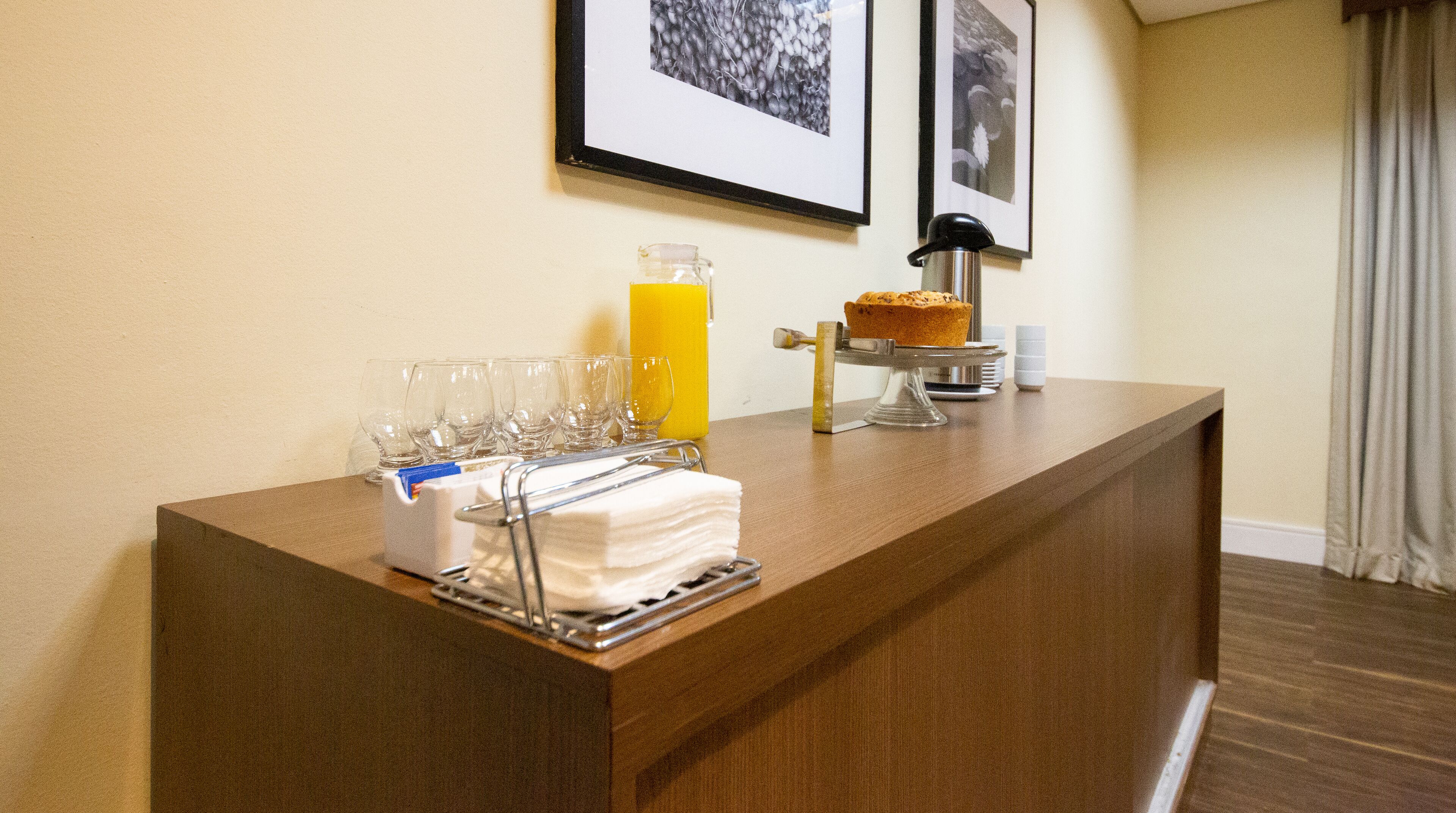 Un comptoir d’accueil d’hôtel avec une pile de serviettes en papier blanches, un pichet en verre rempli de jus d’orange et un gâteau présenté sur un présentoir.
