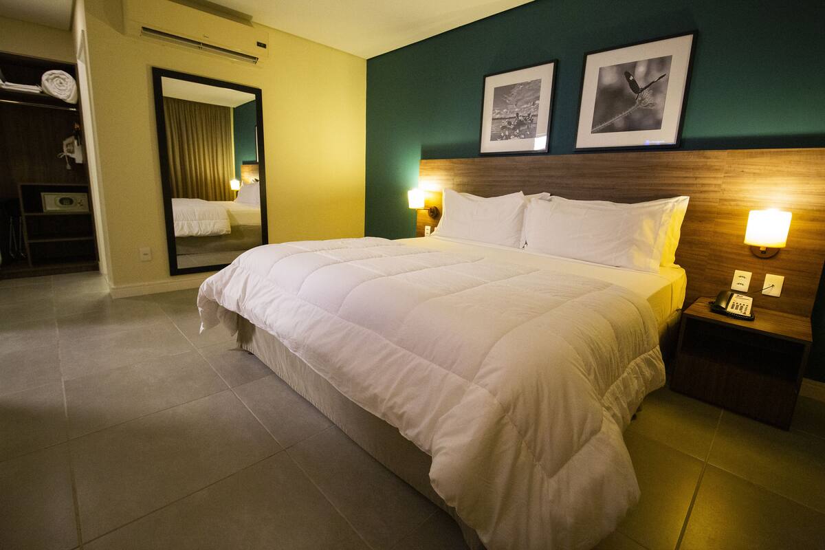 A hotel room with a large bed, a nightstand with a lamp, a mirror, and two framed pictures on the wall.