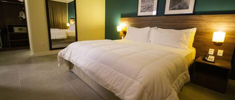 A hotel room with a large bed, a nightstand with a lamp, a mirror, and two framed pictures on the wall.