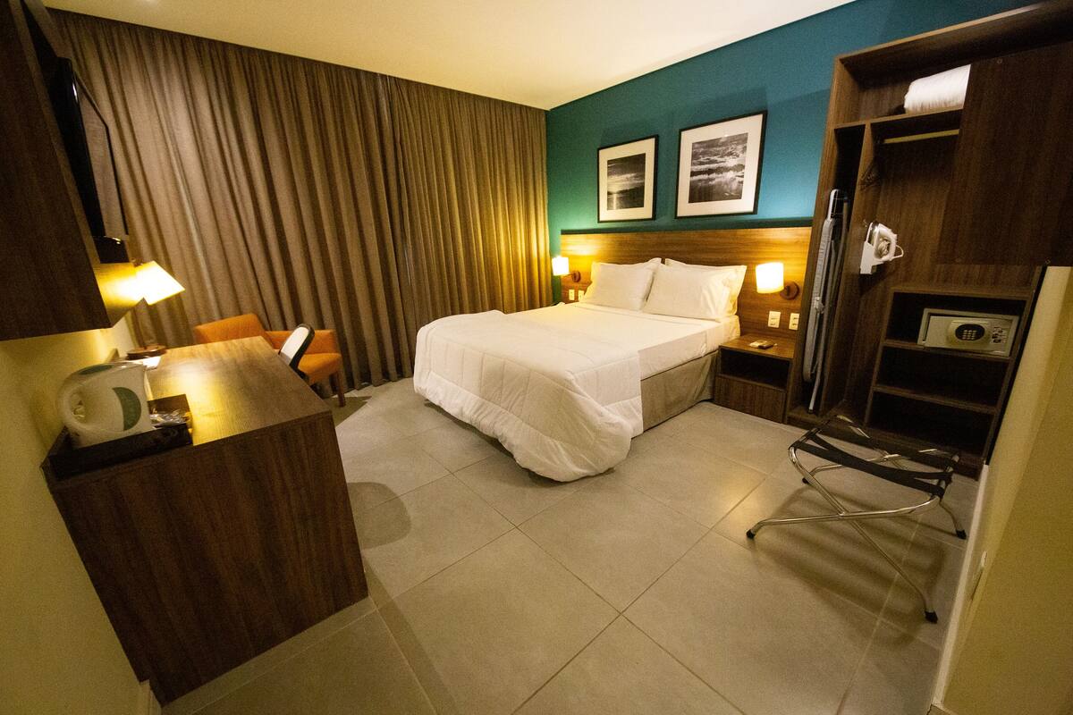 A hotel room with a bed, a desk, a chair, a microwave, and a TV.