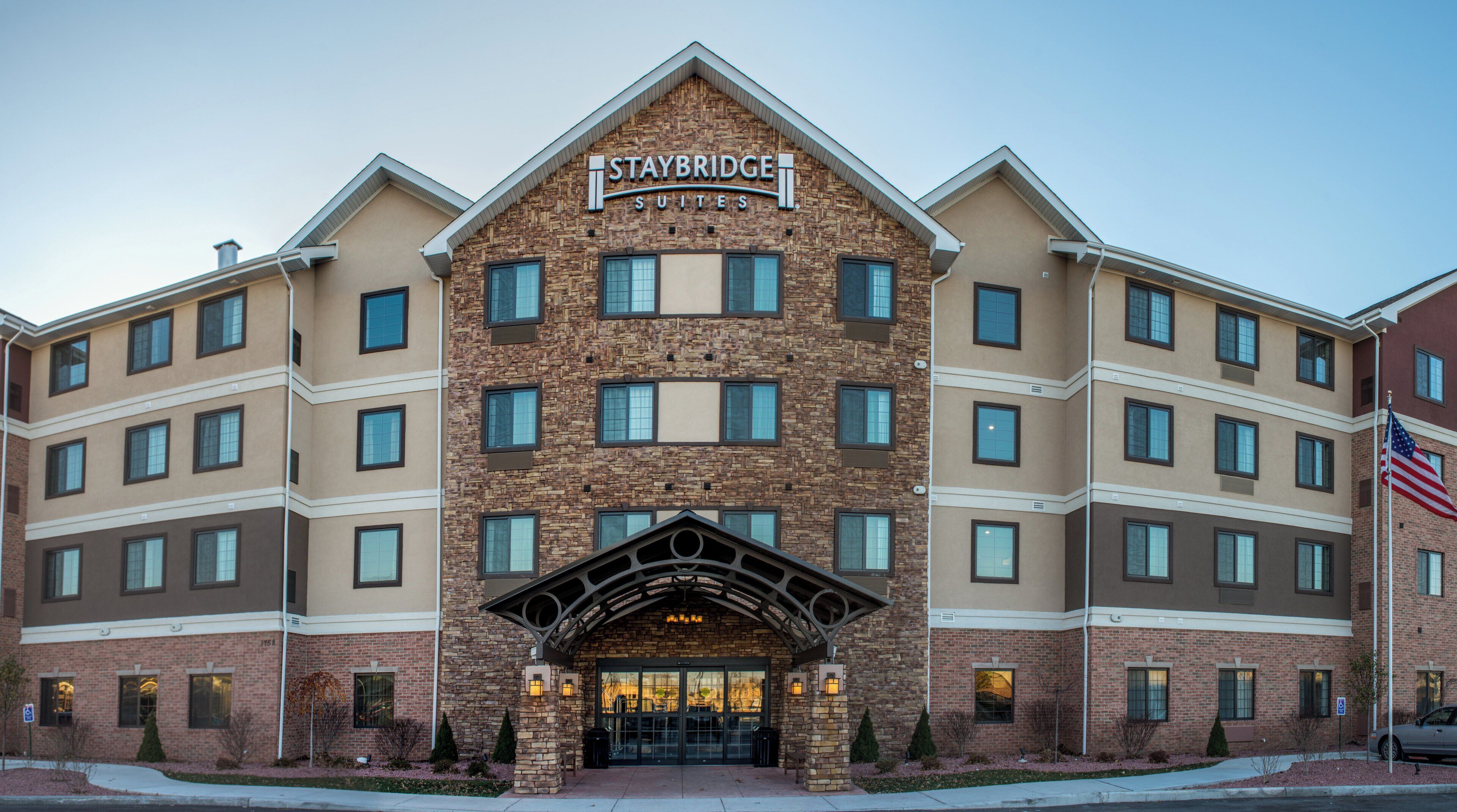A Staybridge Suites hotel with a stone facade, multiple windows, and an American flag.