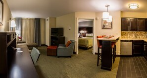 Une chambre d’hôtel équipée d’un bureau, d’une chaise, d’un canapé, d’une télévision, d’une kitchenette et d’une salle de bain.