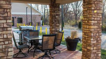 An outdoor patio with a grill, seating, and a view of a brick building.