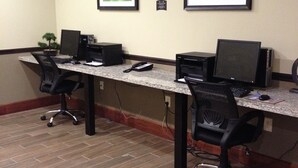A conference room with two desks, each equipped with a computer, keyboard, and mouse. There are two framed pictures on the wall, and a small potted plant on the left side. The room has a tiled floor and a carpeted area near the entrance. - Staybridge Suites Schererville by IHG (Schererville)