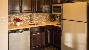 A modern kitchen with dark wooden cabinets, a stainless steel refrigerator, and a tiled backsplash. - Staybridge Suites Schererville by IHG (Schererville)