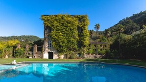 Una piscina con superficie de agua azul cristalina, rodeada por un paisaje verde exuberante y un edificio cubierto de hiedra.