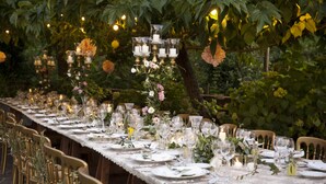 Una larga mesa de comedor dispuesta con copas, platos y velas, rodeada de sillas.