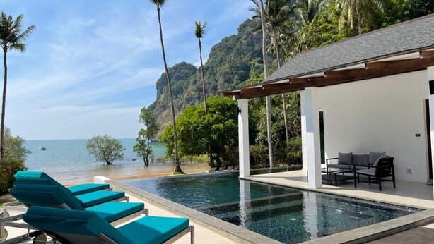 A pool area with lounge chairs, a covered seating area, and a view of the sea and mountains. - The Beach House (Krabi)