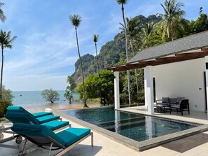 Zona de piscina con sillones de descanso, un espacio de estar cubierto y vistas al mar y a las montañas.