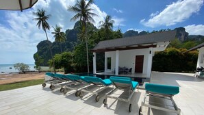 A poolside area with lounge chairs and a covered seating area, overlooking a beach and palm trees. - The Beach House (Krabi)