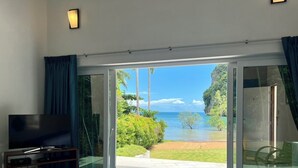 A hotel room with a bed, a TV, and a view of a beach and ocean. - The Beach House (Krabi)