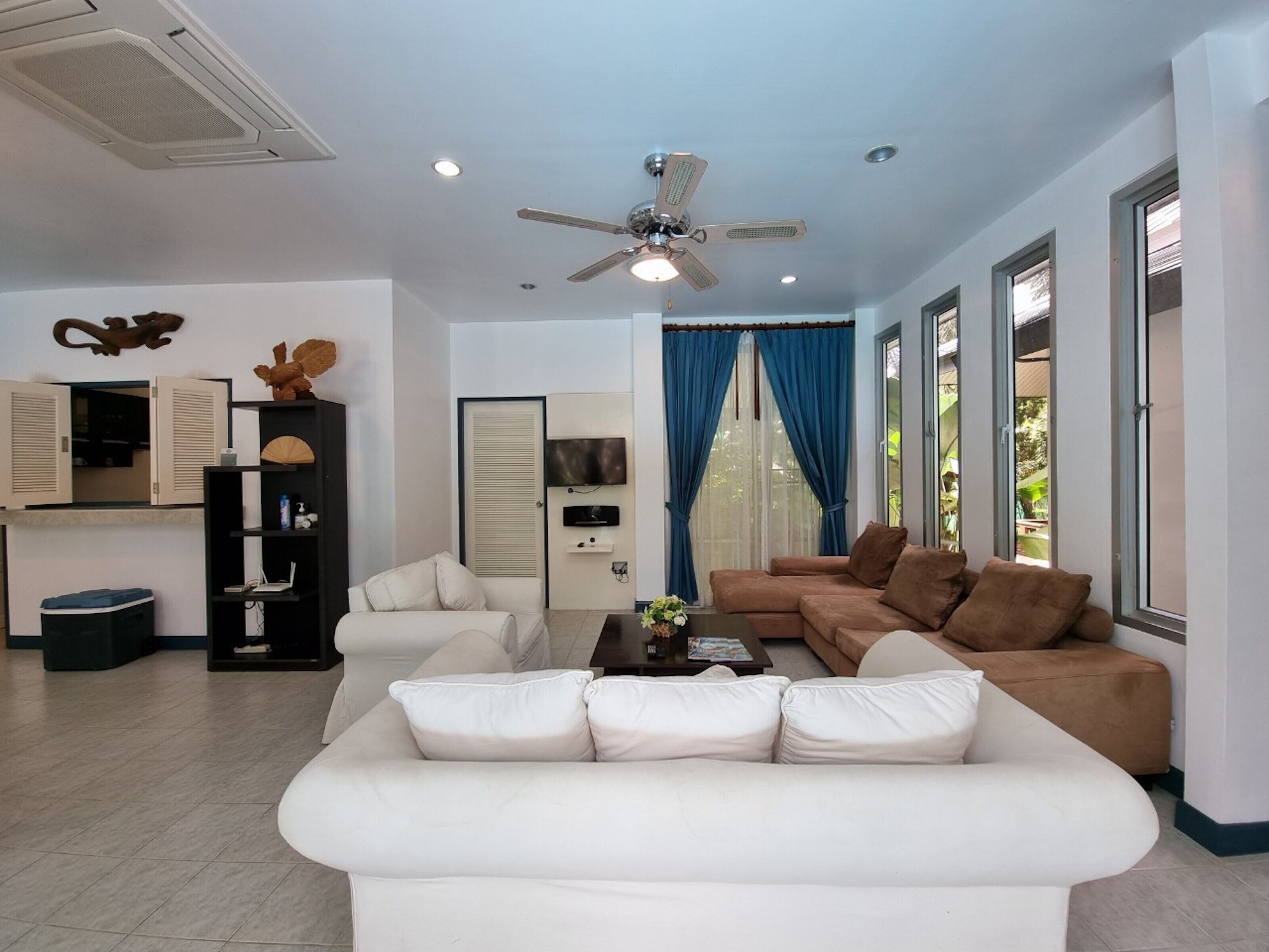 A modern living room with a white sofa, a brown sofa, a ceiling fan, and a TV mounted on the wall.