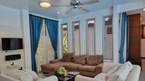 A living room with a brown sofa, white sofa, and a TV mounted on the wall. - Baan Gecko (Krabi)