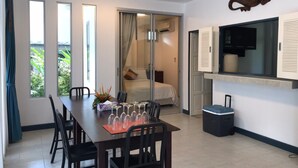 A modern room with a dining table set for six, a bed with a view, a TV, and a small trash bin. - Baan Gecko (Krabi)