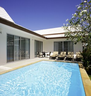 Una casa moderna con piscina, ventanas amplias y mobiliario de exterior.