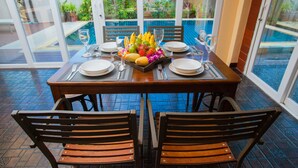 A dining table set for four with a tropical fruit centerpiece, surrounded by chairs. - Baan Manu Chang (Krabi)