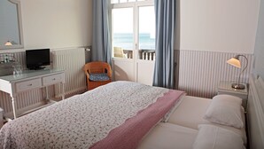 Une chambre d’hôtel avec un lit, un bureau avec une télévision, une chaise et une vue sur la mer par la fenêtre.