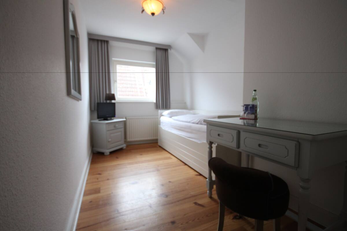 A small, neatly arranged bedroom with a bed, bedside table, and a desk with a chair.