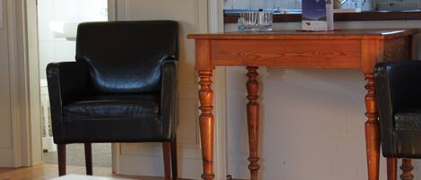 Una habitación con una mesa de madera, dos sillas de cuero negro, una mesa blanca y un salpicadero de azulejos al fondo.