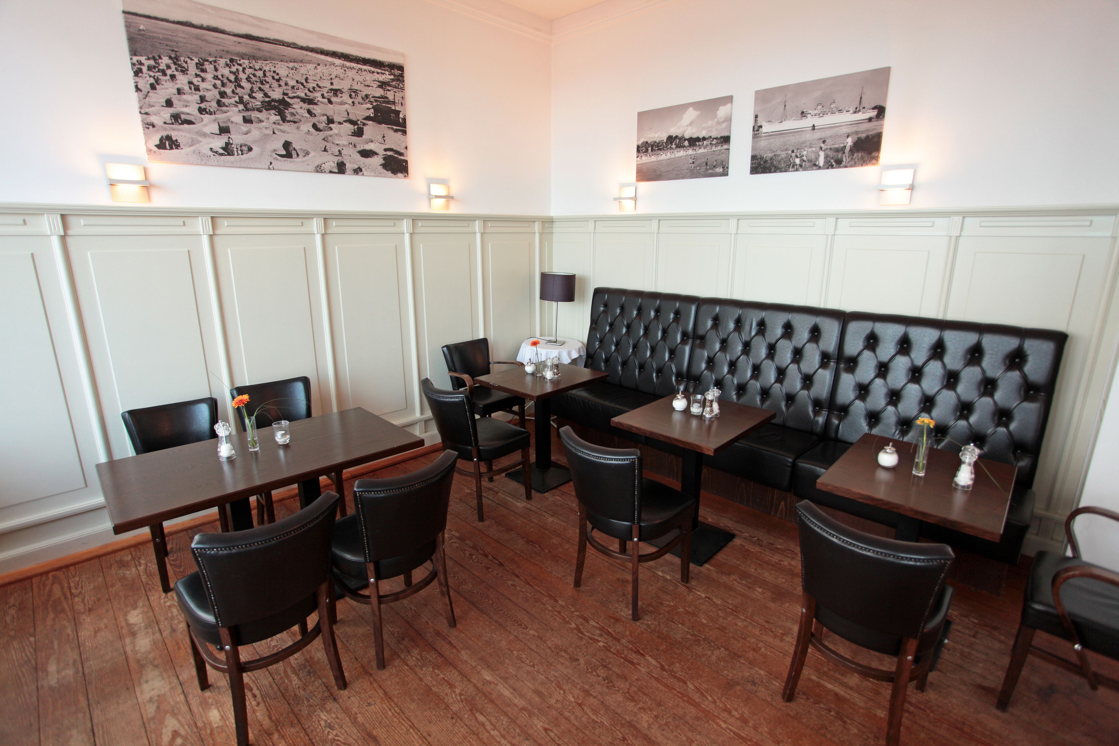 A restaurant with wooden tables and black leather chairs, a black cushioned bench, and wall-mounted light fixtures.