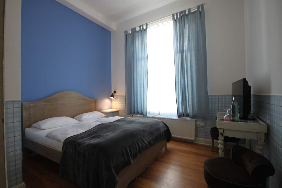 A bedroom with a bed, a nightstand, a TV, and a window with curtains.