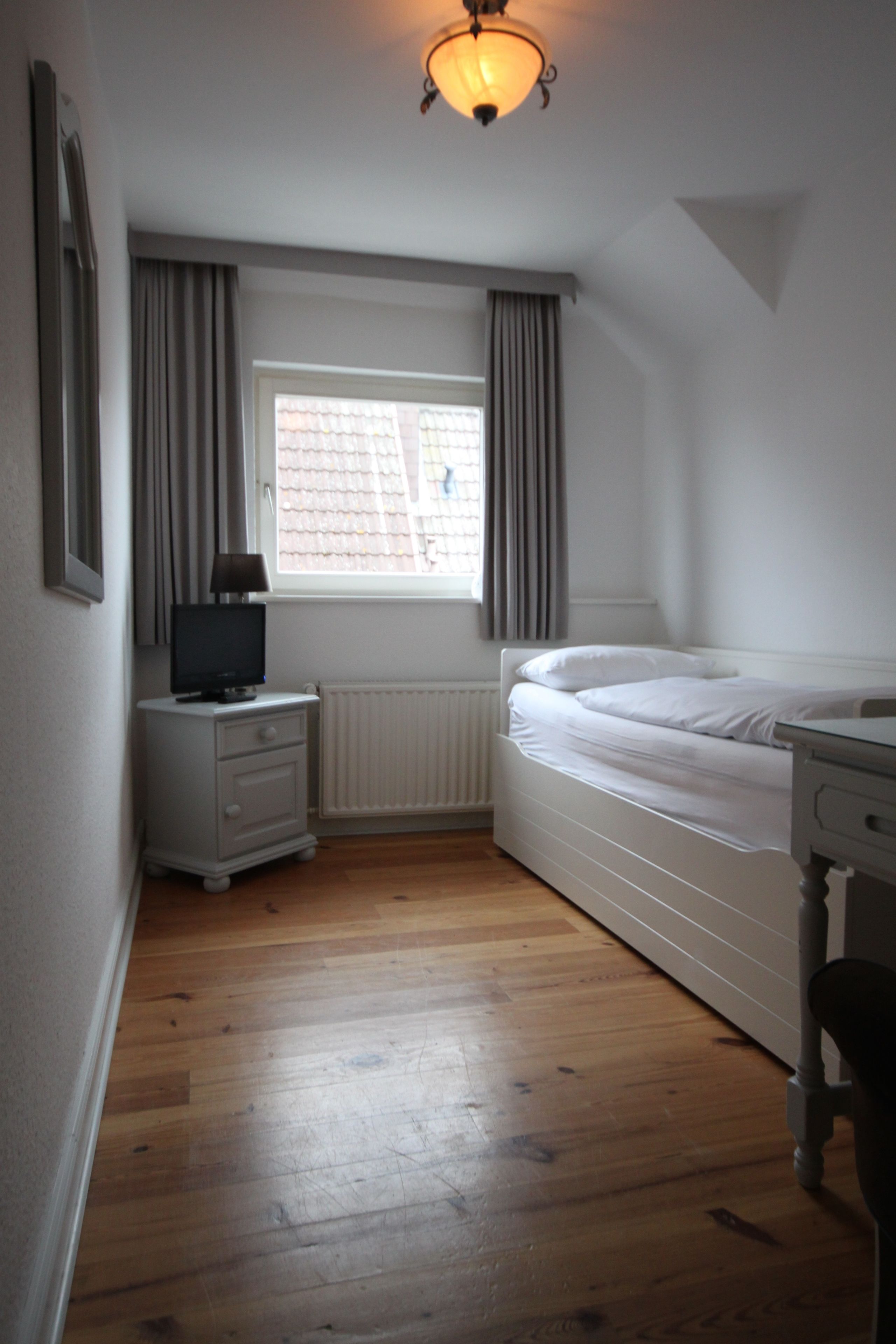 A small, clean room with a single bed, a bedside table, a TV, and a window with curtains.