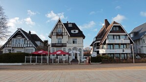 Un bâtiment de style européen traditionnel, doté d’une entrée centrale, de deux balcons et d’un parasol rouge au-dessus de l’entrée.