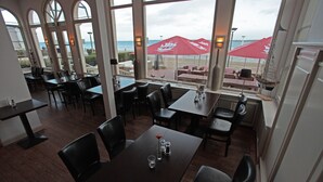 Un restaurant doté de grandes baies vitrées donnant sur la plage, et proposant une terrasse avec des parasols.